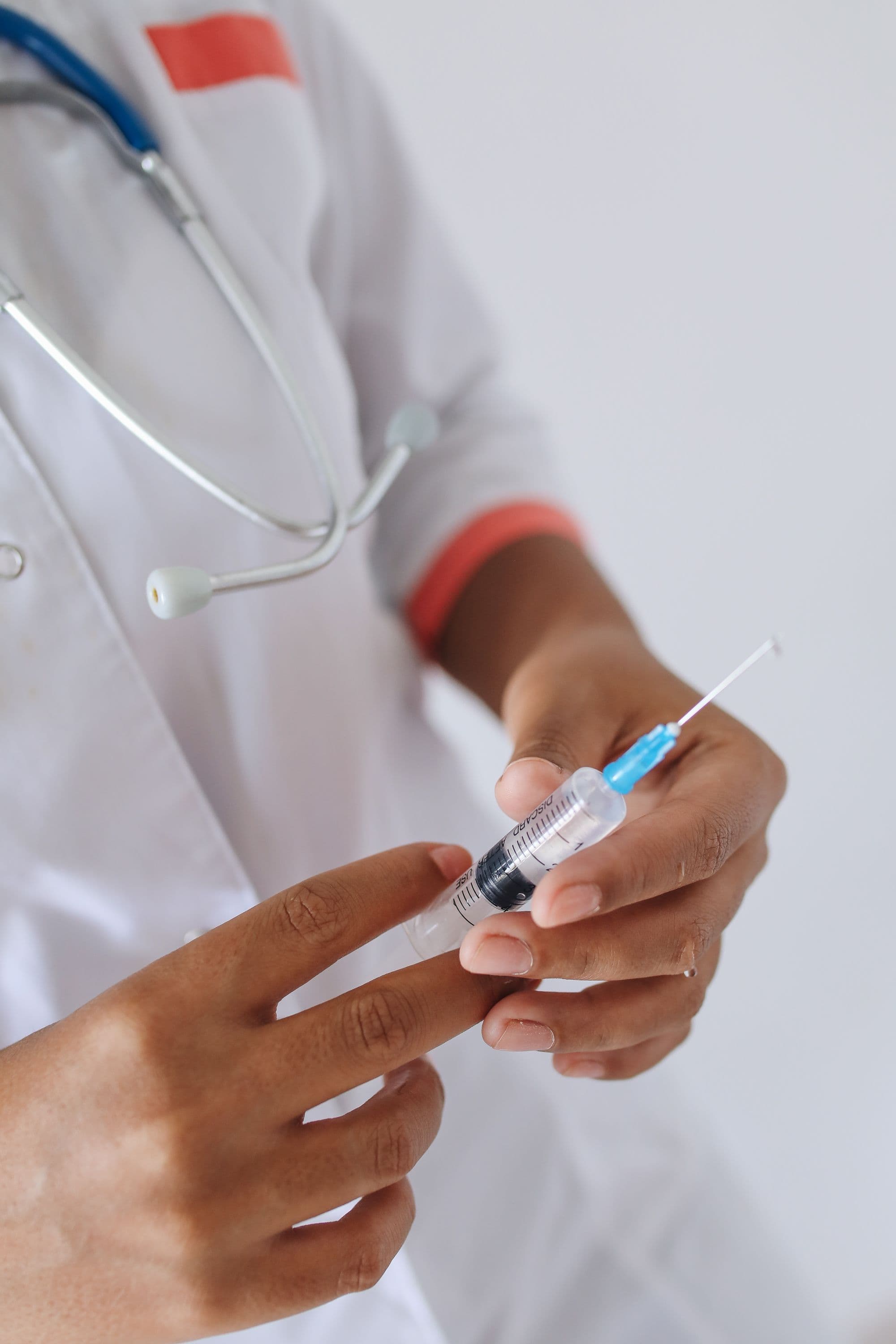 Healthcare professional preparing a syringe with a stethoscope visible.